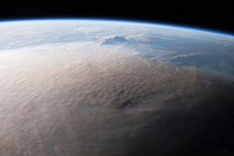 Vista dall'alto della Terra con una curva chiaramente visibile e un pennacchio grigio-marrone che copre la maggior parte della superficie visibile.